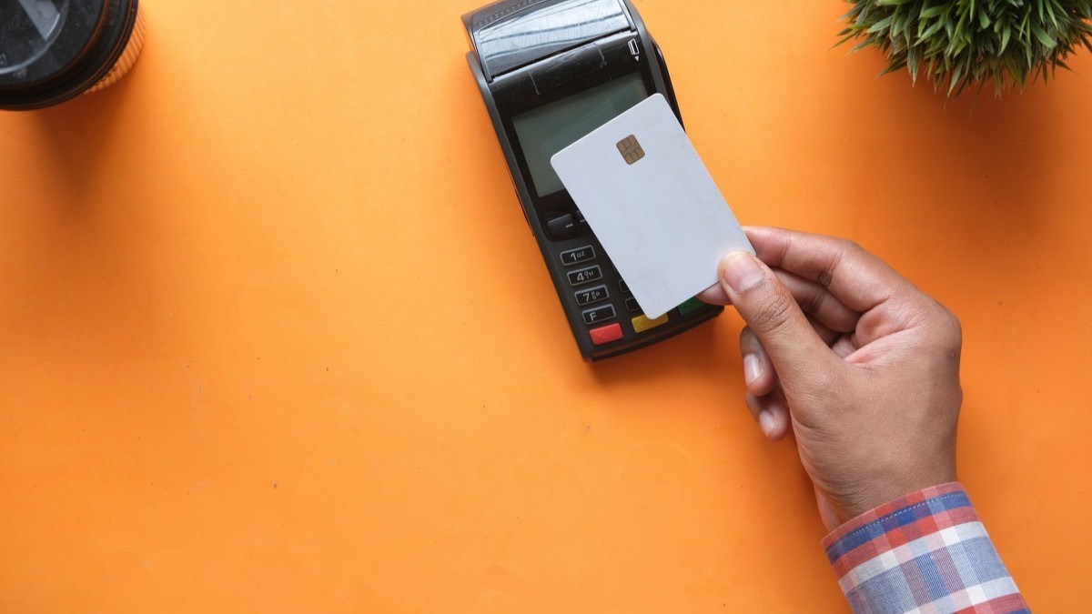 A hand holding a blank, unbranded chip card up to a payment terminal